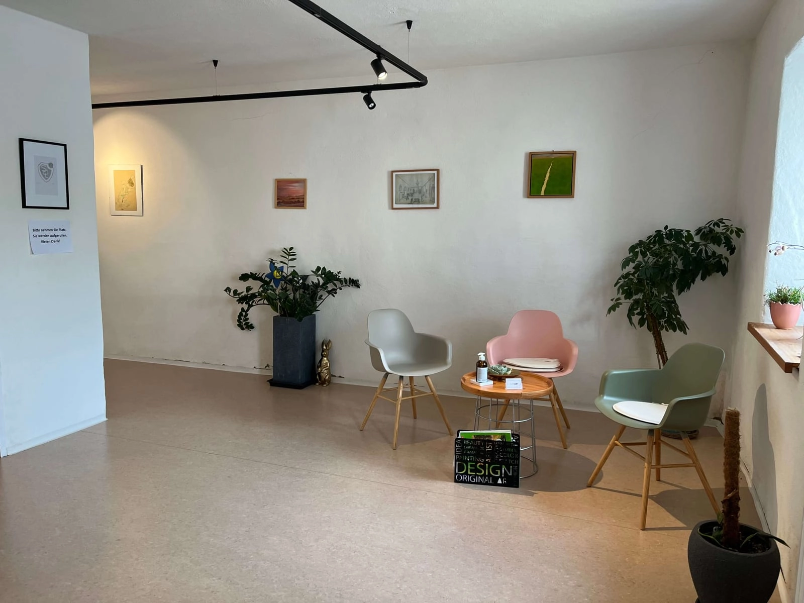 Wartebereich mit hellen Sesseln, Zimmerpflanzen und gerahmten Bildern an der Wand